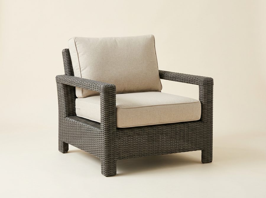 Fauteuil de jardin en résine tressée gris foncé, larges accoudoirs, coussins d’assise et de dossier beige clair