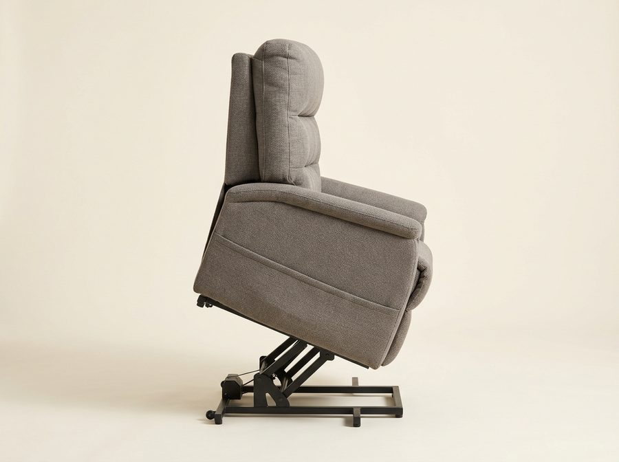 Fauteuil releveur en tissu taupe vu de profil, assise soulevée et basculée vers l’avant sur son châssis en acier